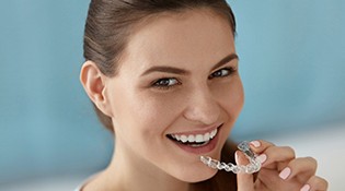 A young woman smiling as she prepares to insert a clear aligner into the top arch of her smile